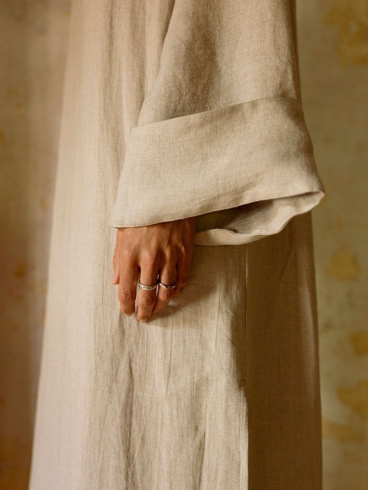 A hand resting at the turned-back cuff of a natural linen sleeve
