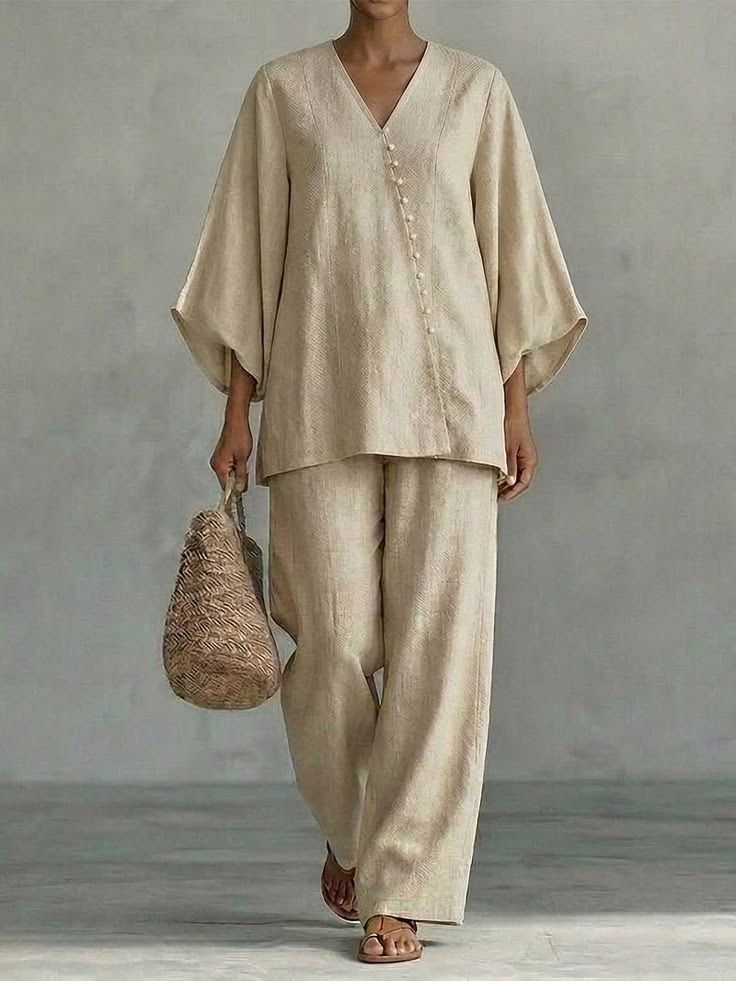 Woman in a sand linen tunic with wide sleeves and matching trousers, carrying a woven bag